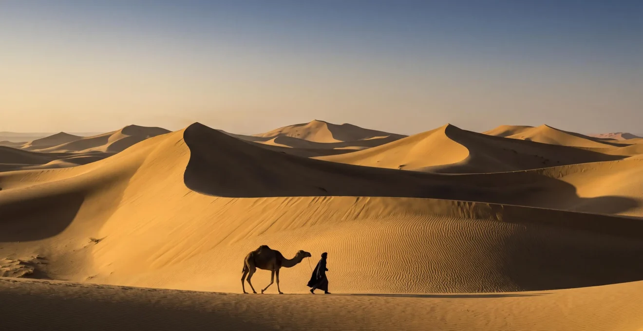 Vast golden desert dune sea at sunrise with a small robed figure and camel silhouette emphasizing the scale between human culture and desert geography
