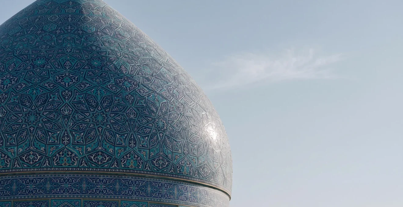 Sweeping editorial view of Isfahan's iconic blue-tiled mosque dome under a clear sky, its geometric mosaic patterns shimmering in natural light.